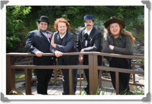 The men of the cast stand on a bridge. They are all wearing suits. Landon has a fake moustache.